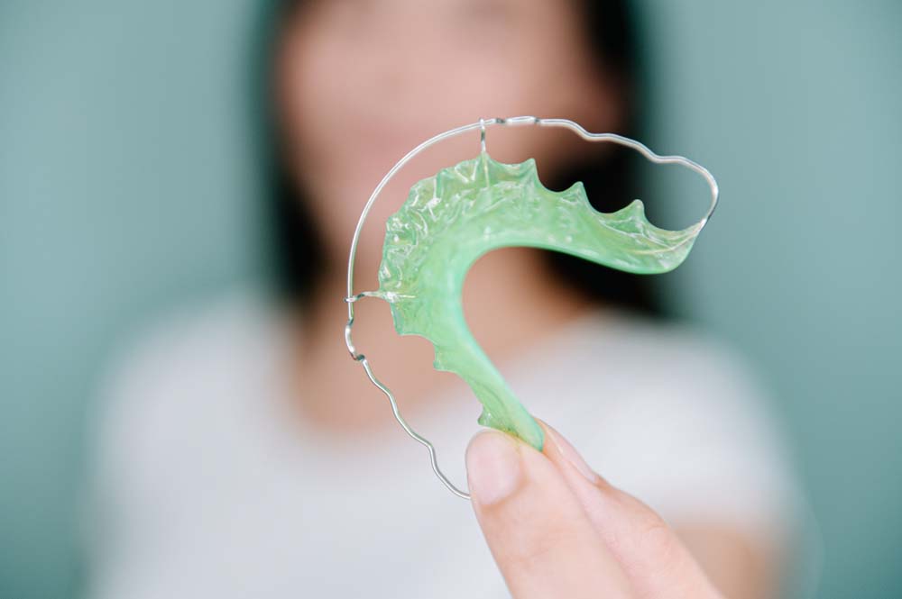 teenage girl holding her green wire retainer
